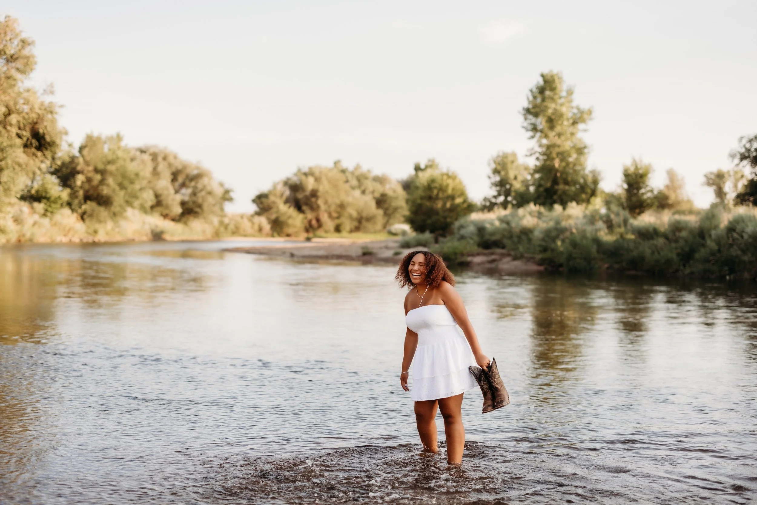 Girl holding cowboy boots while standing in a river.