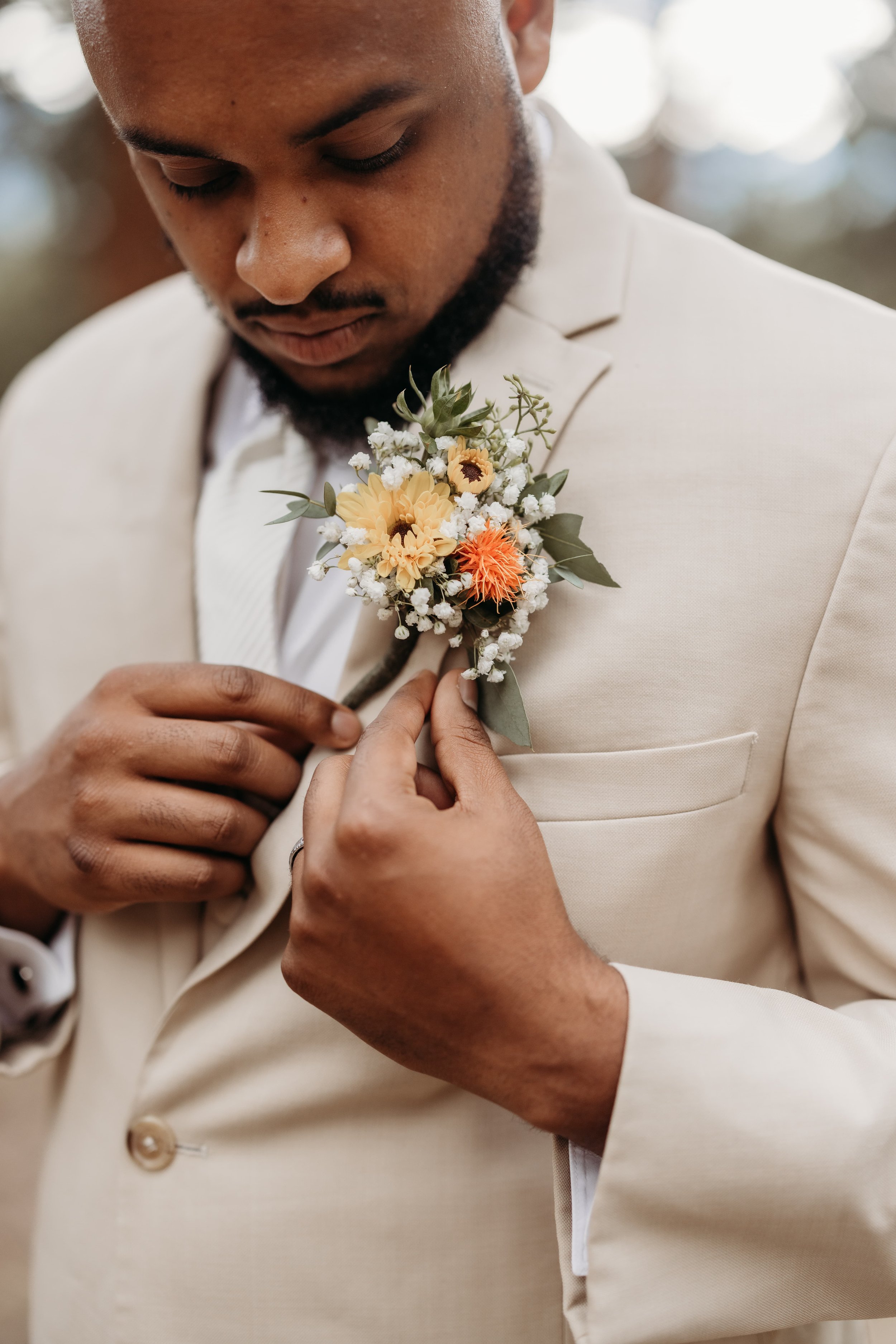 Groom in a tan suit adjusting his colorful boutonniere.