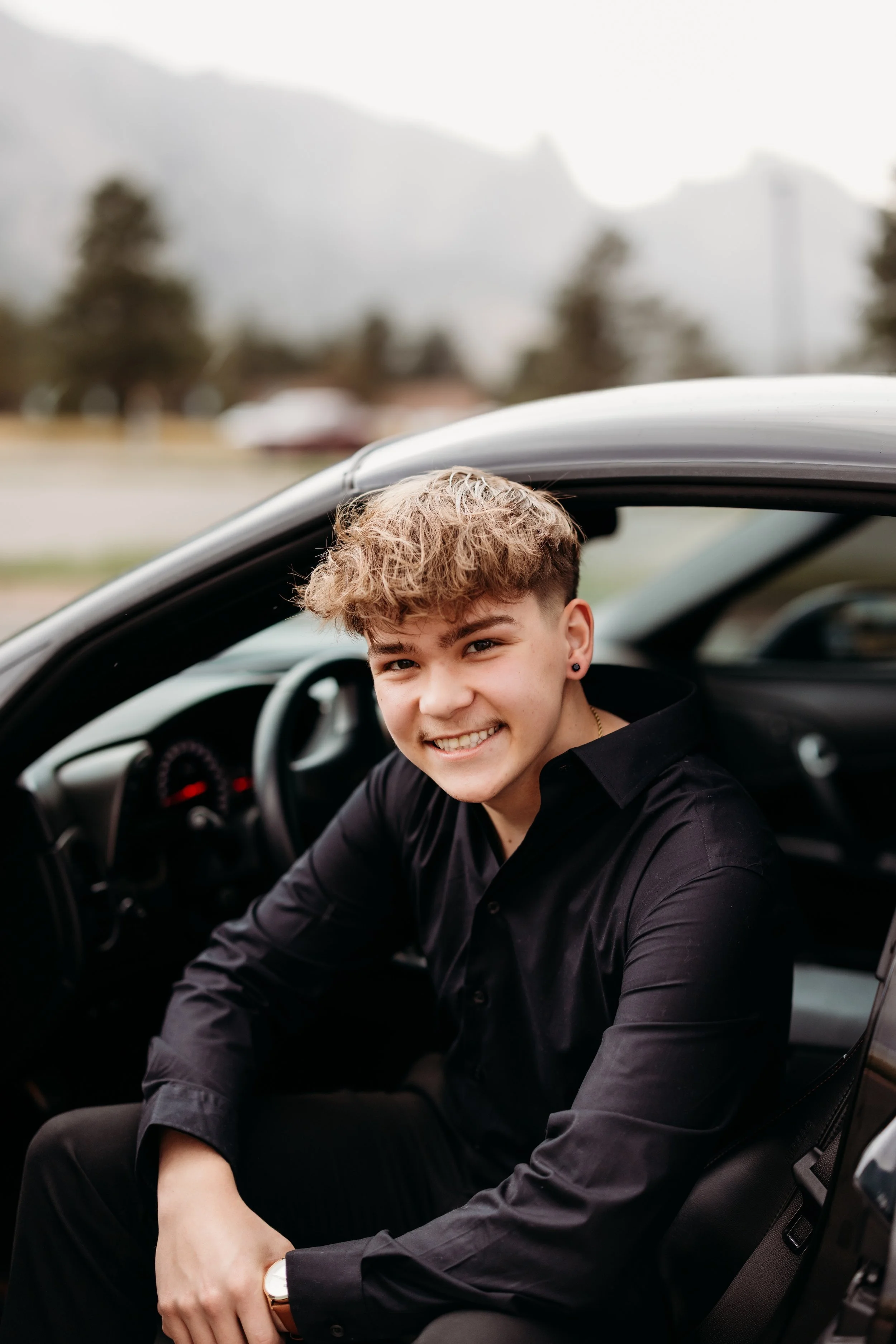 Senior boy sitting and smiling in the driver's seat of his car.