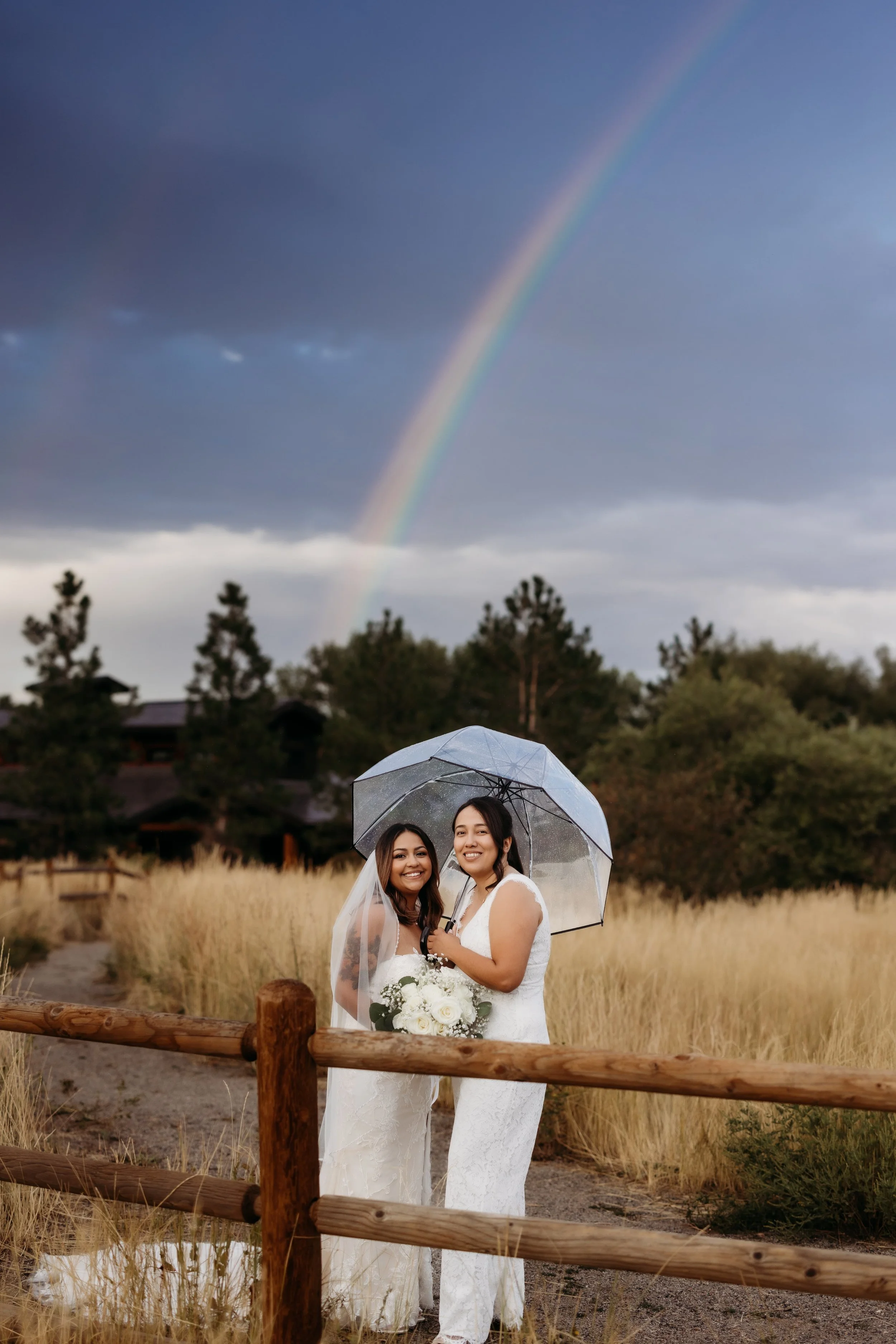 Two brides smiling beneath a rainbow during their Boulder, Colorado elopement.
