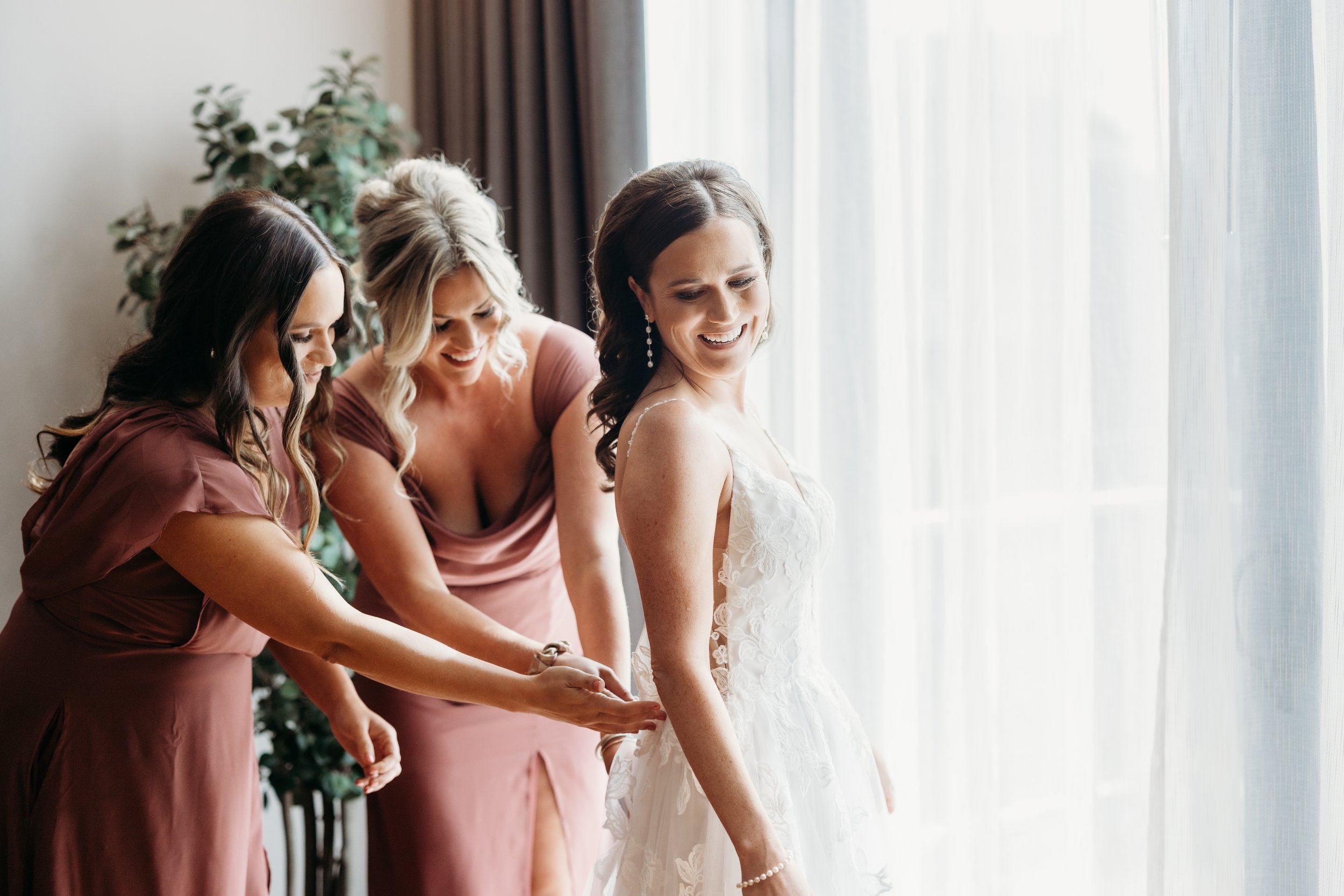 Two bridesmaids zipping up the bride's wedding dress.