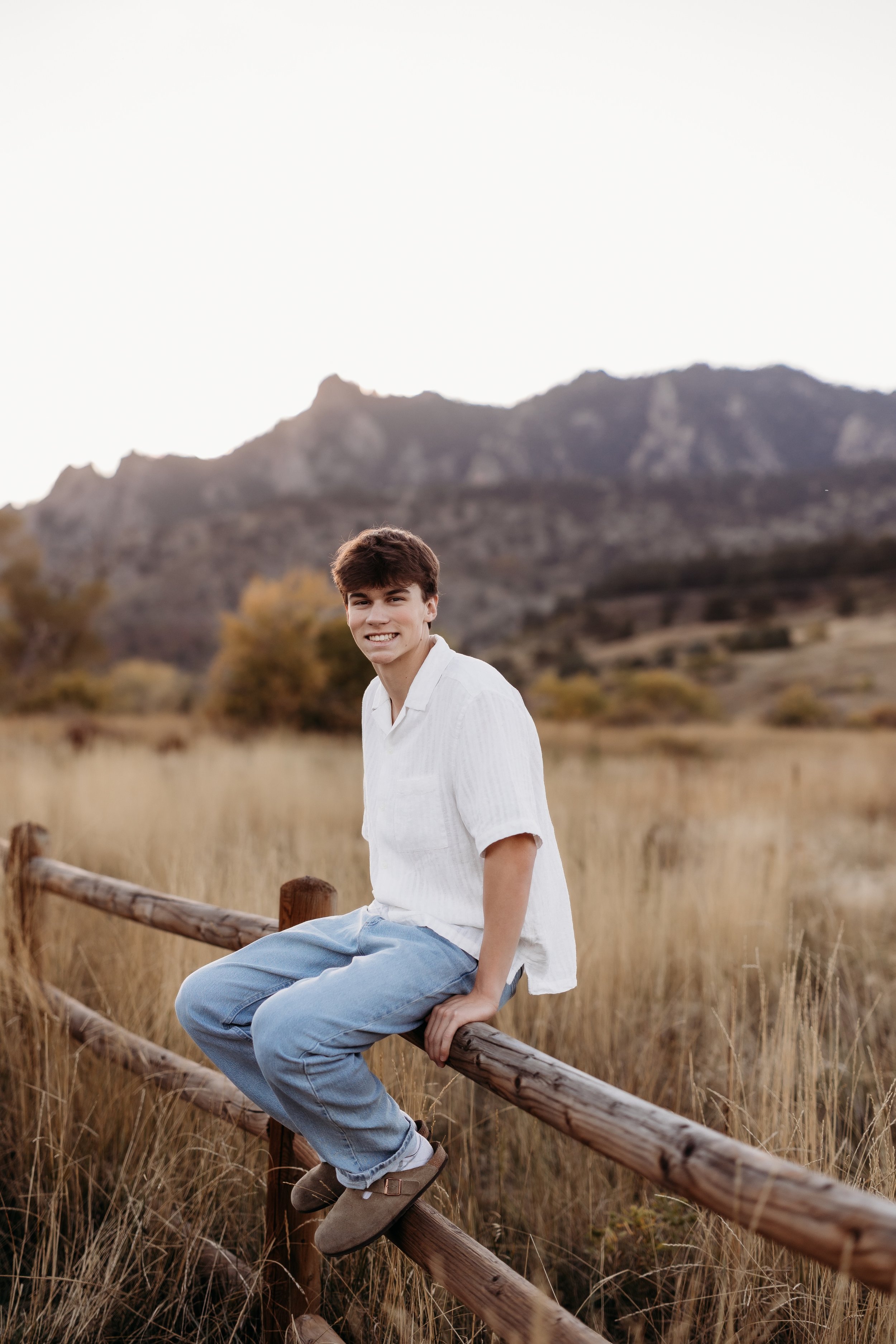 Senior boy sitting on a fence in Boulder, Colorado.