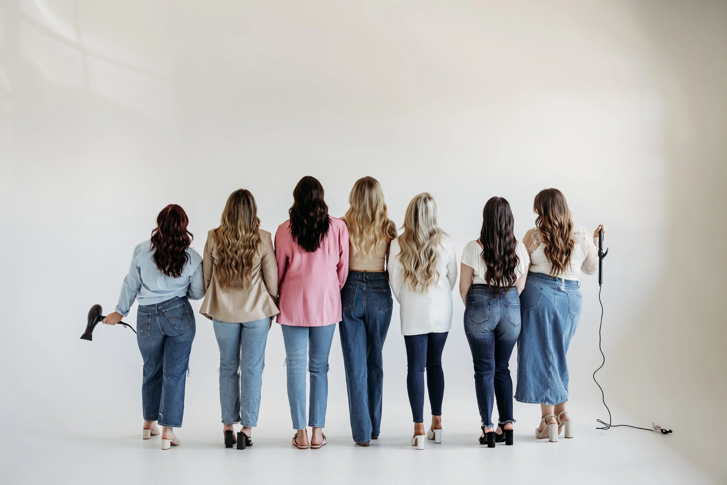 Seven women facing away from the camera in front of a white background.