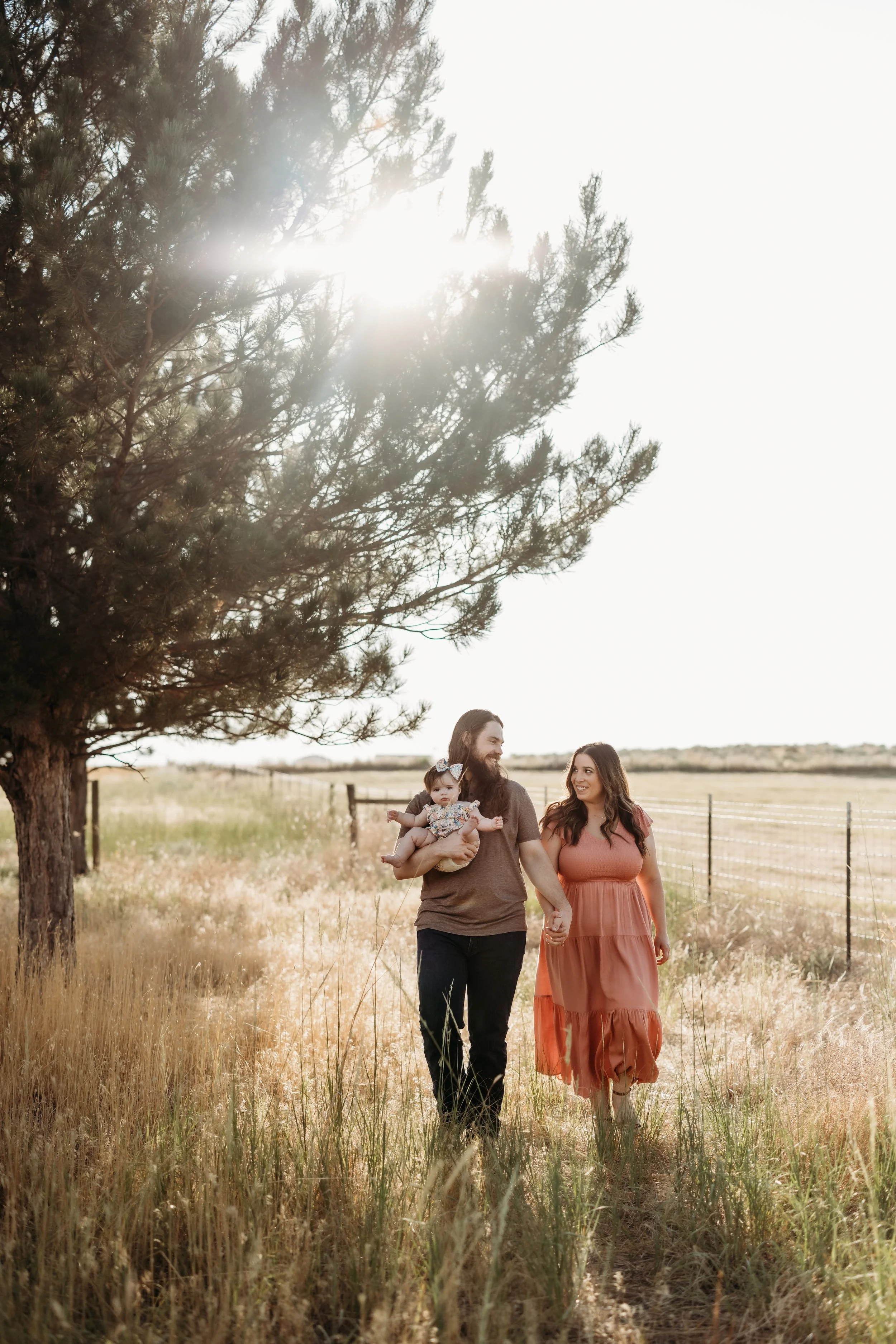 Man holding a toddler girl while holding hands and walking with his wife.