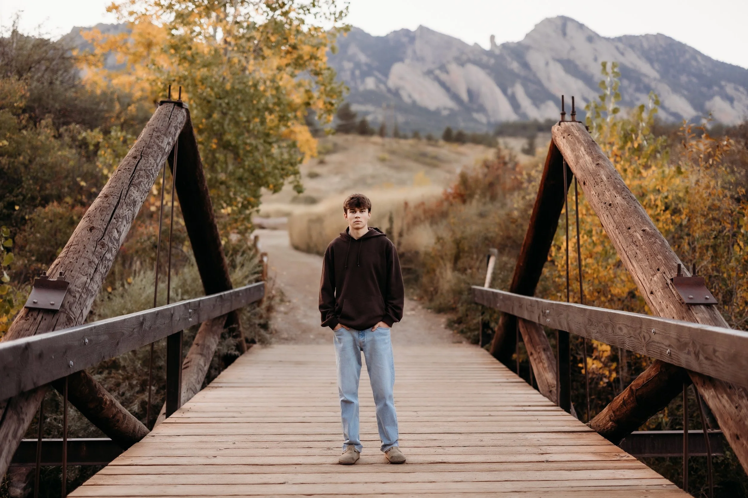 Boy posing on a wooden bridge with mountains behind him.