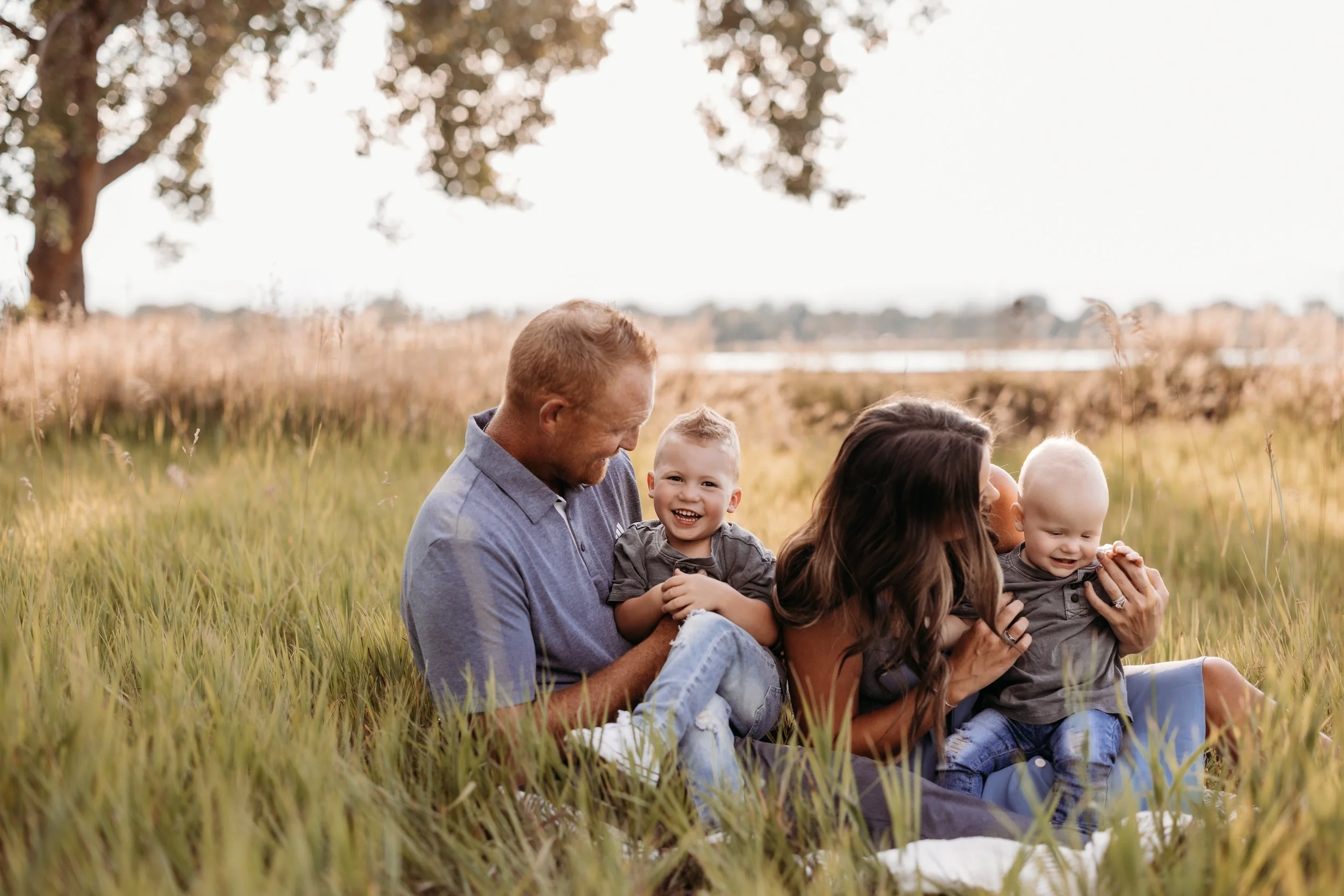 Family of four sitting in a field and laughing.