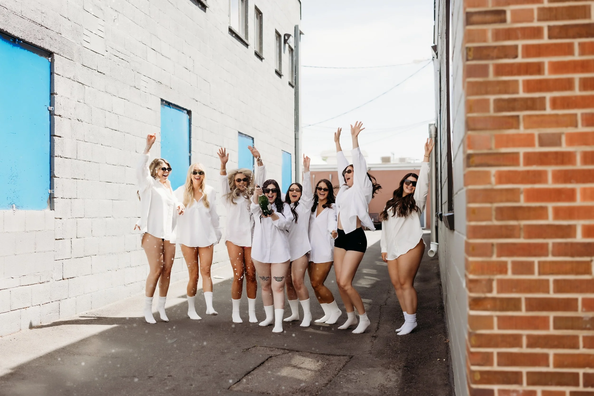 Eight women in white button ups and socks jumping in an alley.