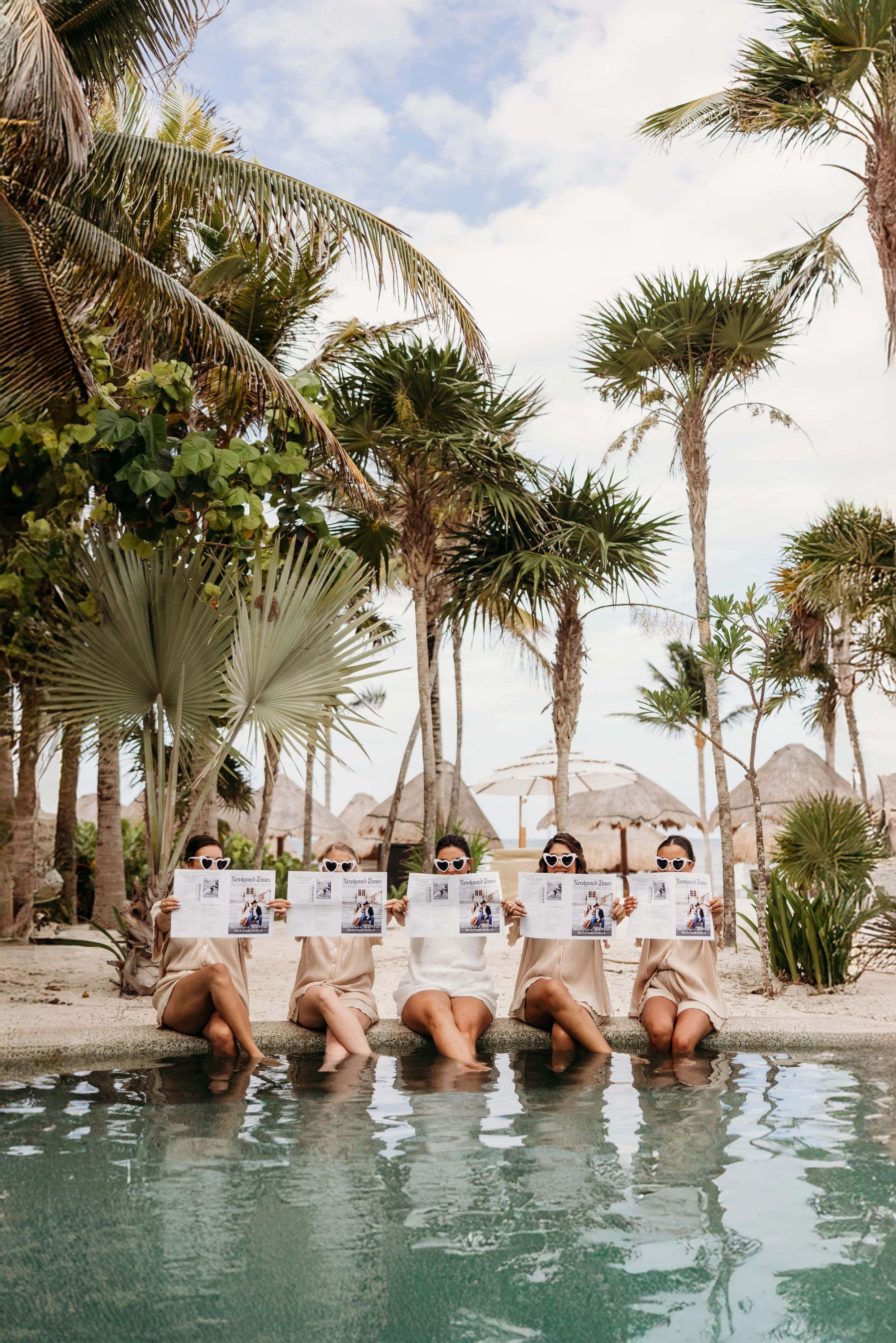 Bride and bridesmaids reading the newspaper at a pool in Cancun.