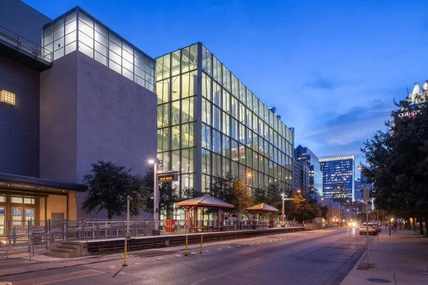 Modern glass building on city street during evening with trees and streetlights.
