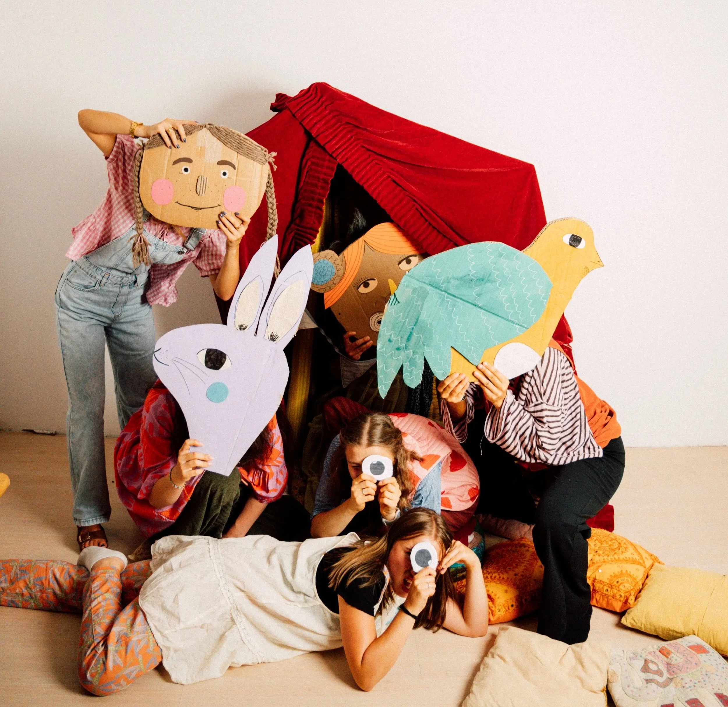 Menschen bei einer Puppenmusik-Performance mit Masken und Handpuppen, die Tiere und Fantasiefiguren darstellen, im Raum mit weißen Wänden.