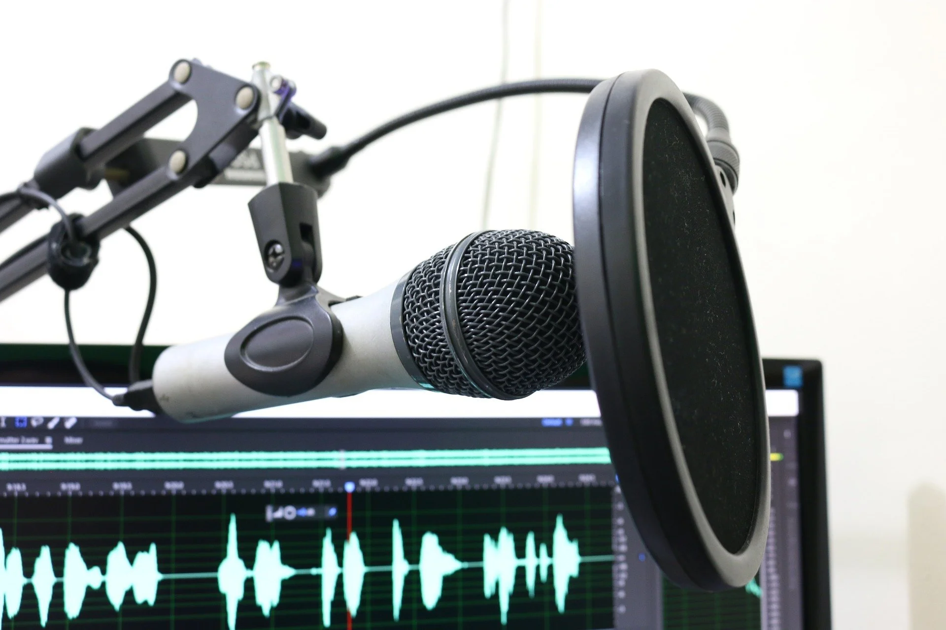 Close-up of a microphone with a pop filter in front of a computer screen displaying audio waveform.