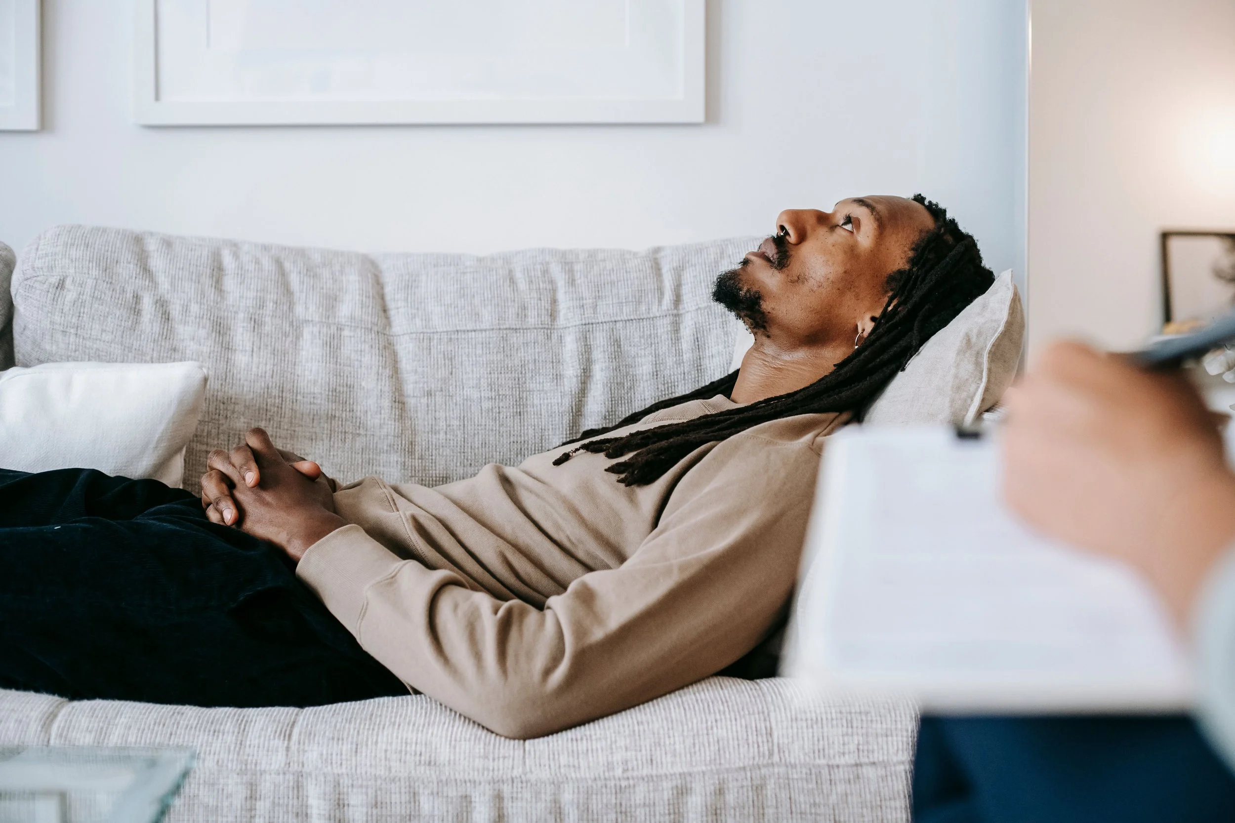 Man with dreadlocks and beard lying on a couch, looking up.