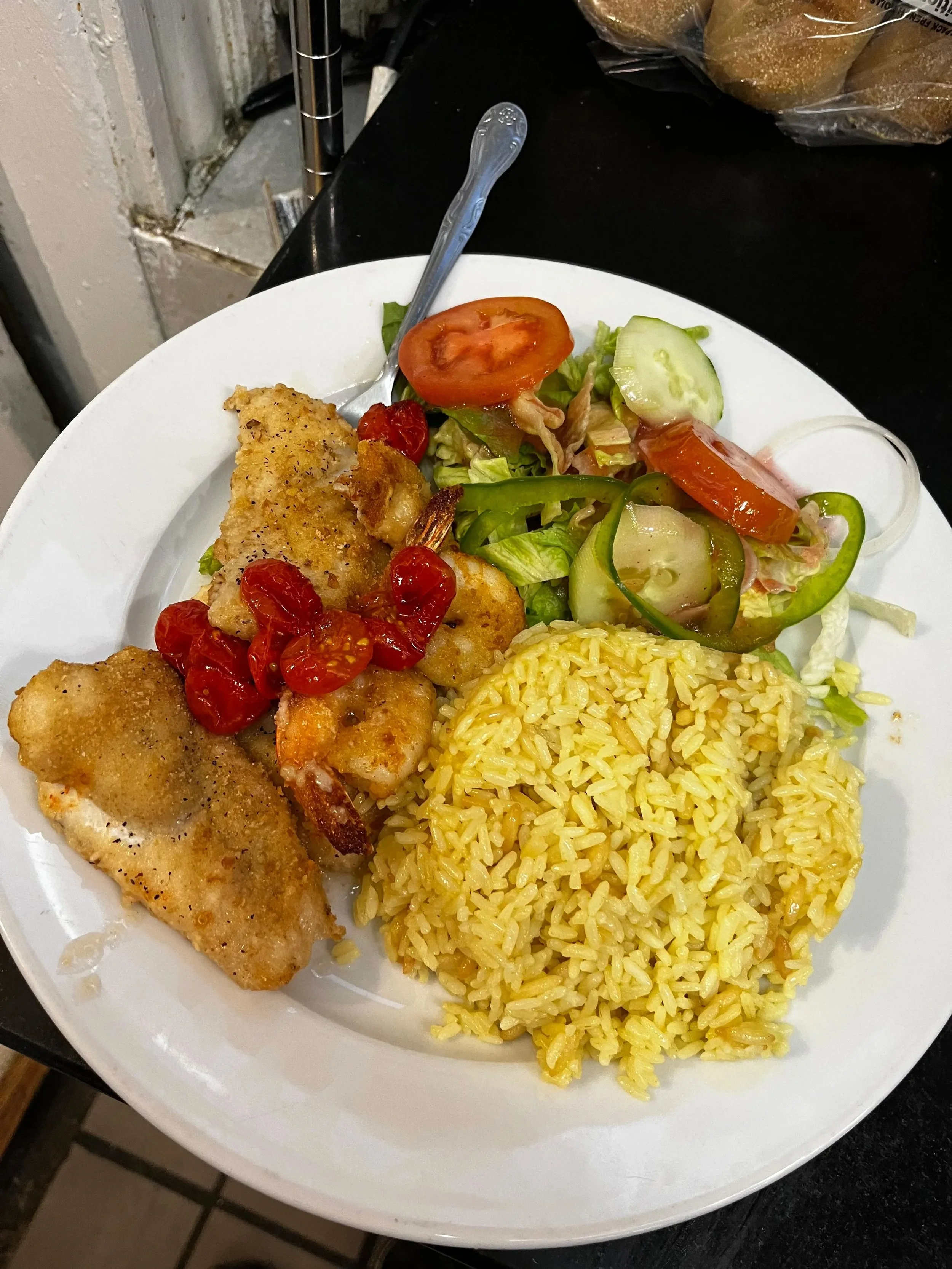 Plate with fried fish, yellow rice, and a green salad with tomatoes and cucumbers.