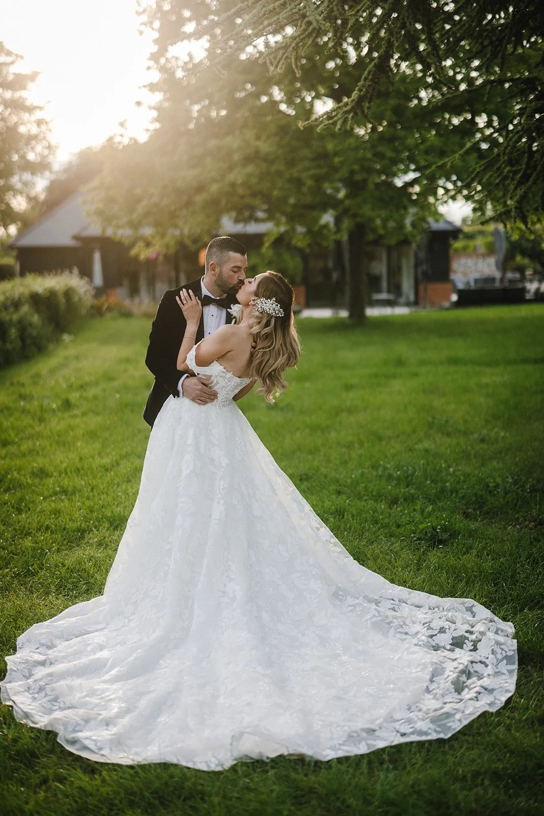 A bride and groom share a kiss outdoors on a green lawn, couple