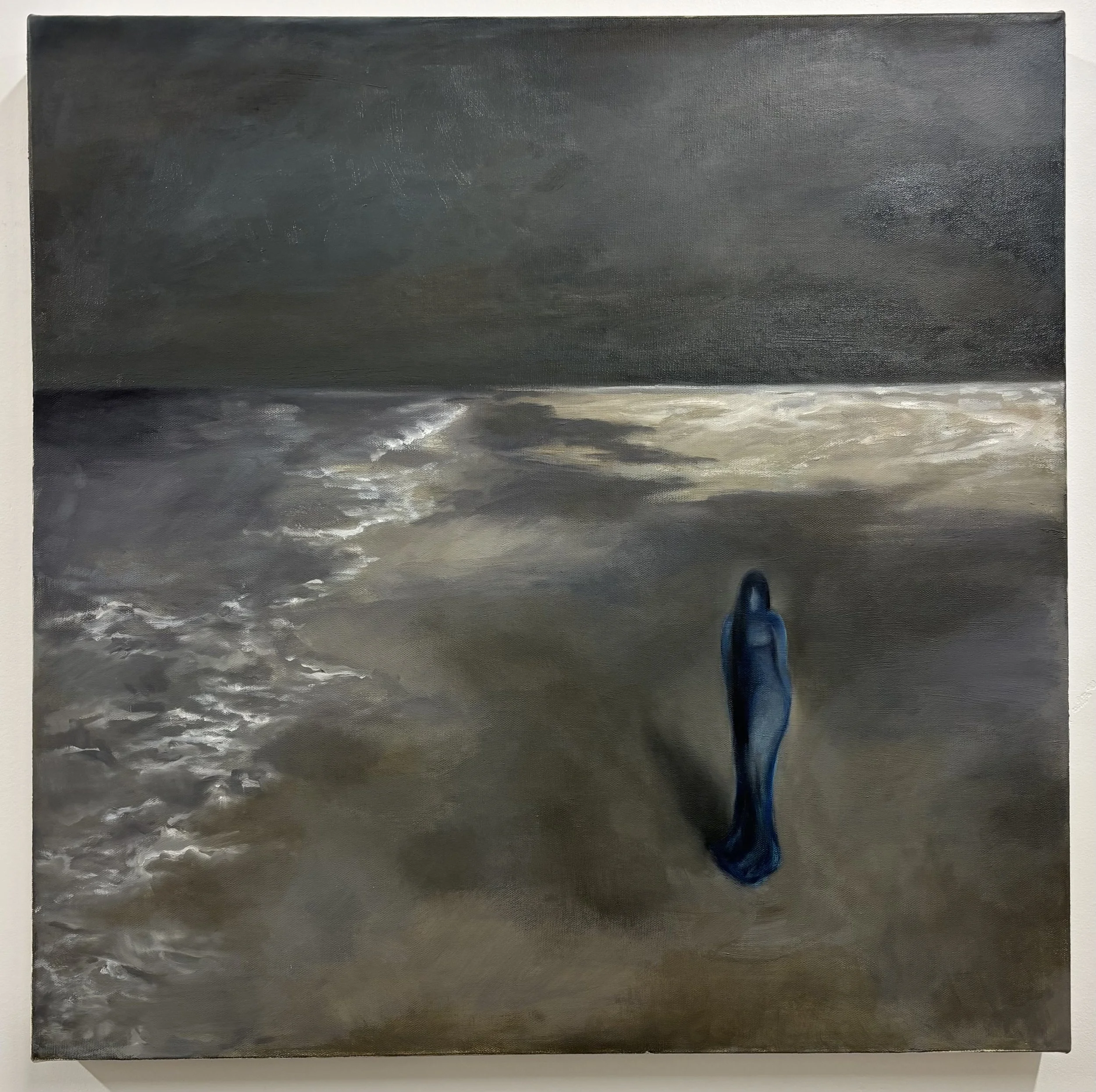 A dark, stormy sky over the ocean with waves crashing onto the shore. In the foreground, a person's blue shoe is visible at the bottom of the image.