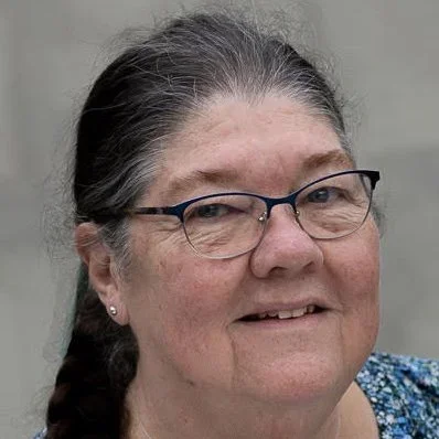 Close-up of a woman with glasses and gray hair in a braid, smiling.