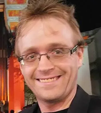 A young man with glasses smiling at the camera