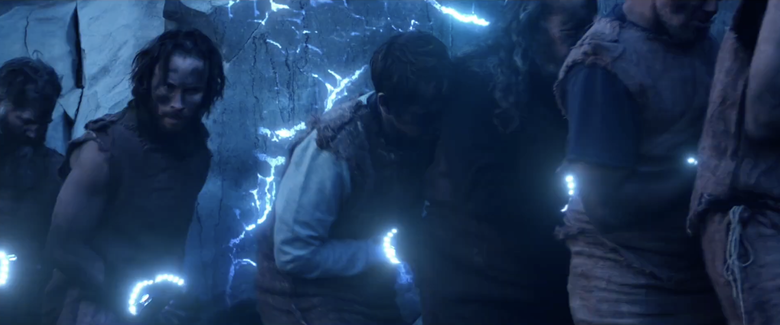 Scene from the movie 'Indiana Jones and the Dial of Destiny' showing characters navigating a dark, rocky environment with glowing blue lights and electrical sparks.