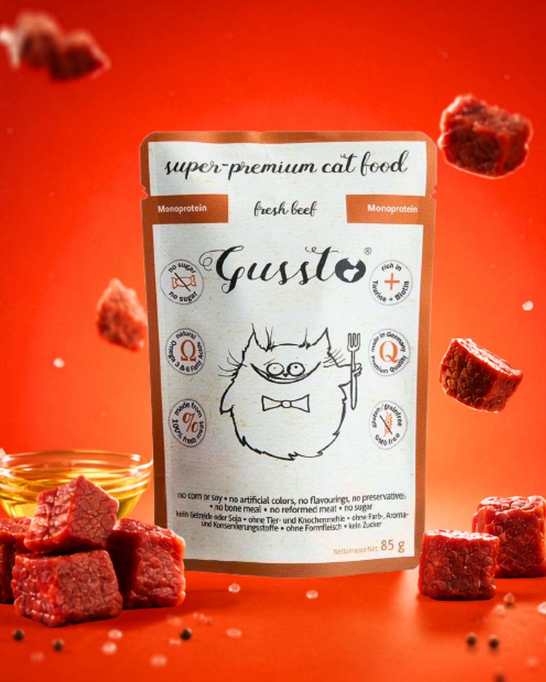 Package of super-premium cat food with a cartoon cat illustration, surrounded by pieces of raw meat and a small bowl of oil, set against a red background.