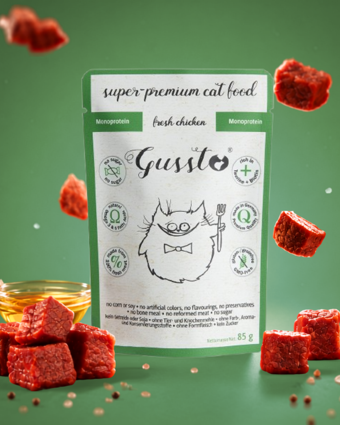 Package of super-premium cat food labeled Garcinia with illustrations of raw meat cubes and unprocessed ingredients, set against a green background with scattered raw meat cubes and small grains.