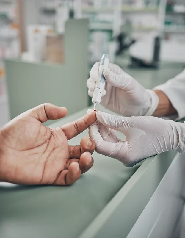 Eine Apothekerin führt einen Bluttest an einem Finger eines Patienten durch, der im medizinischen Umfeld sitzt.