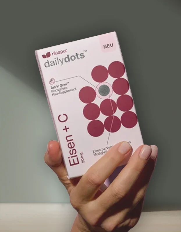 Hand hält eine Packung Nicapur Daily Dots with Eisen + C. Verpackung ist weiß mit rotem Design und roten Punkten.