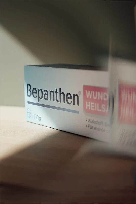 Eine Packung Bepanthen Salbe auf einem Holztisch, teilweise im Schatten, mit klarer Sicht auf das Label.