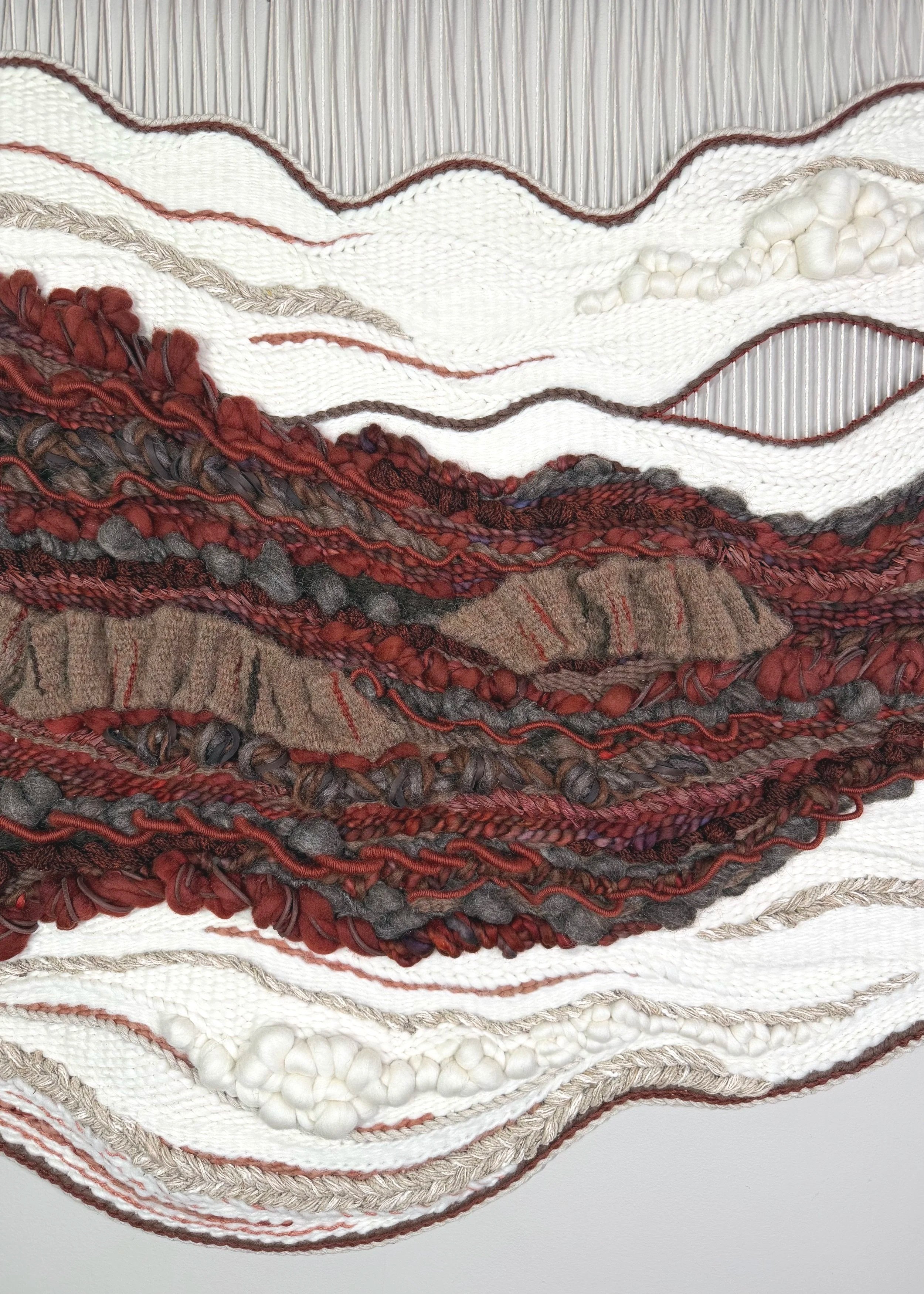 Close-up of a textured textile art piece with various layers of woven, knotted, and yarn elements in earth tones.