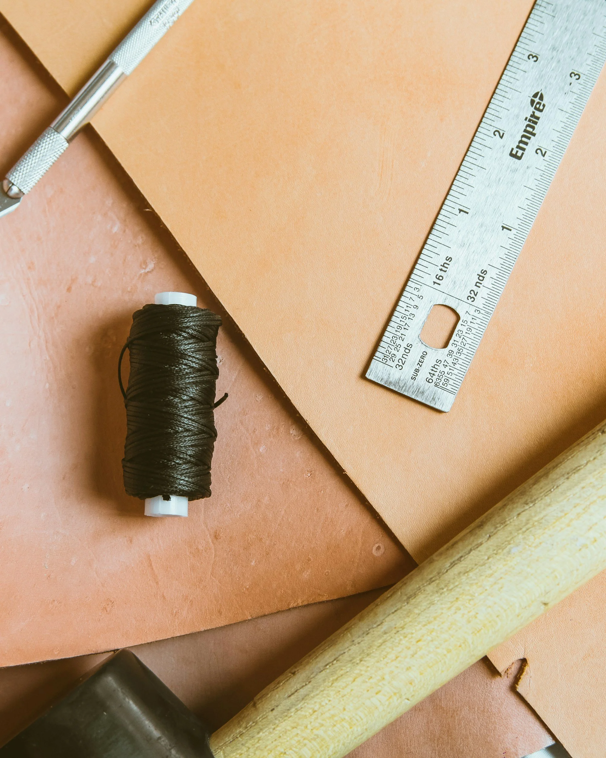 A mechanical pencil, a roll of black thread, a metal ruler, a piece of paper, and a wooden stick are arranged on a brown surface.