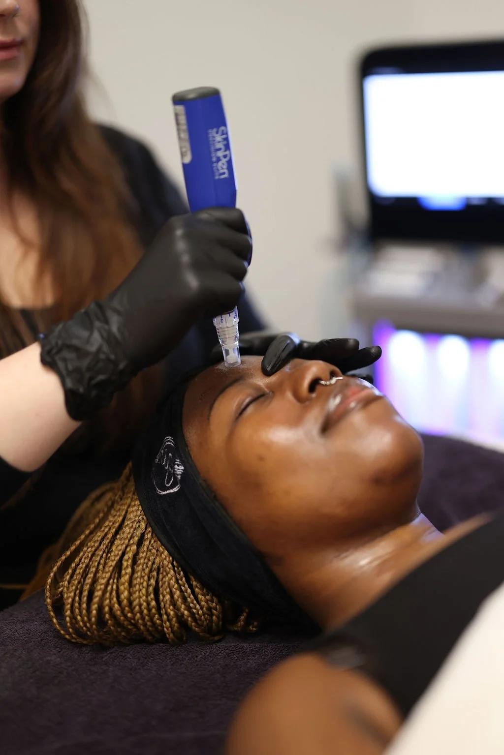 A woman receiving a SkinPen treatment on forehead from a healthcare professional wearing black gloves.