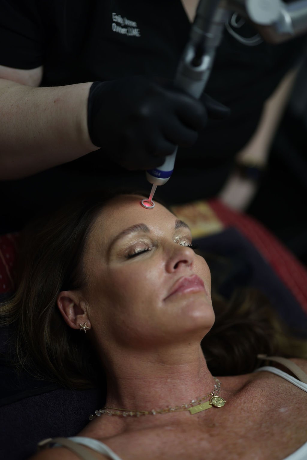 A woman receiving treatment on her forehead from a medical professional wearing black gloves.
