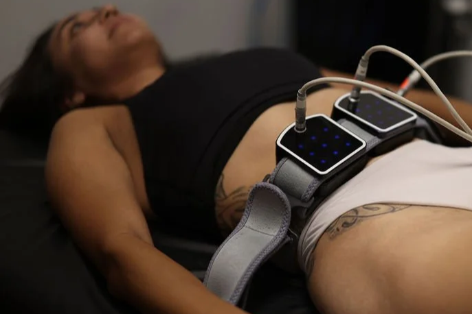 A woman lying on her back with a belt around her waist, attached to two electronic devices, and wires connected to them.
