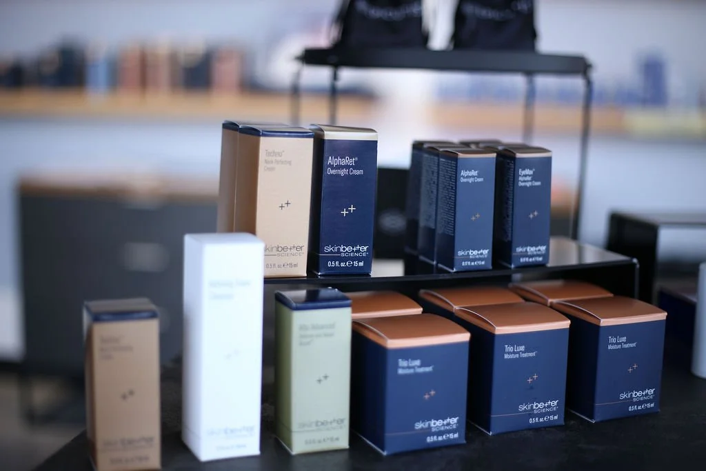 Display of skincare products on a black table, including boxed creams labeled AlphaRet Overnight Cream, Triple Luxe Moisture Treatment, and others from SkinBetter Science, with a blurred background.