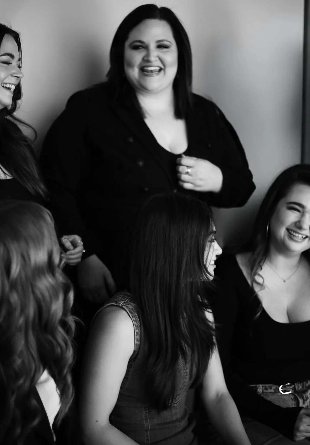 A group of five women laughing and talking in a casual indoor setting, black and white photograph.