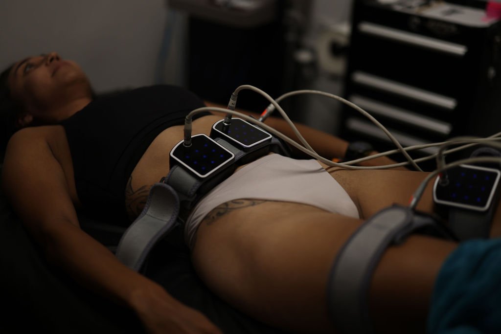 A woman lying down with electrodes attached to her abdomen for body contouring treatment.