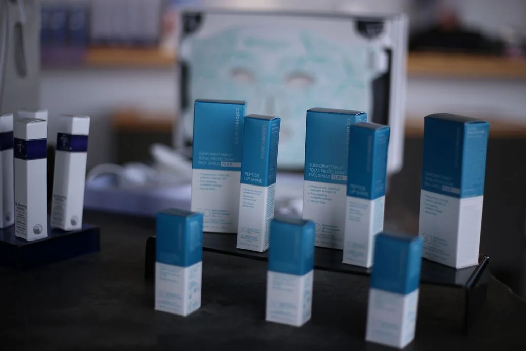 Various boxes of skincare or medical products, mainly in blue and white packaging, are displayed on a dark surface with a blurred background.