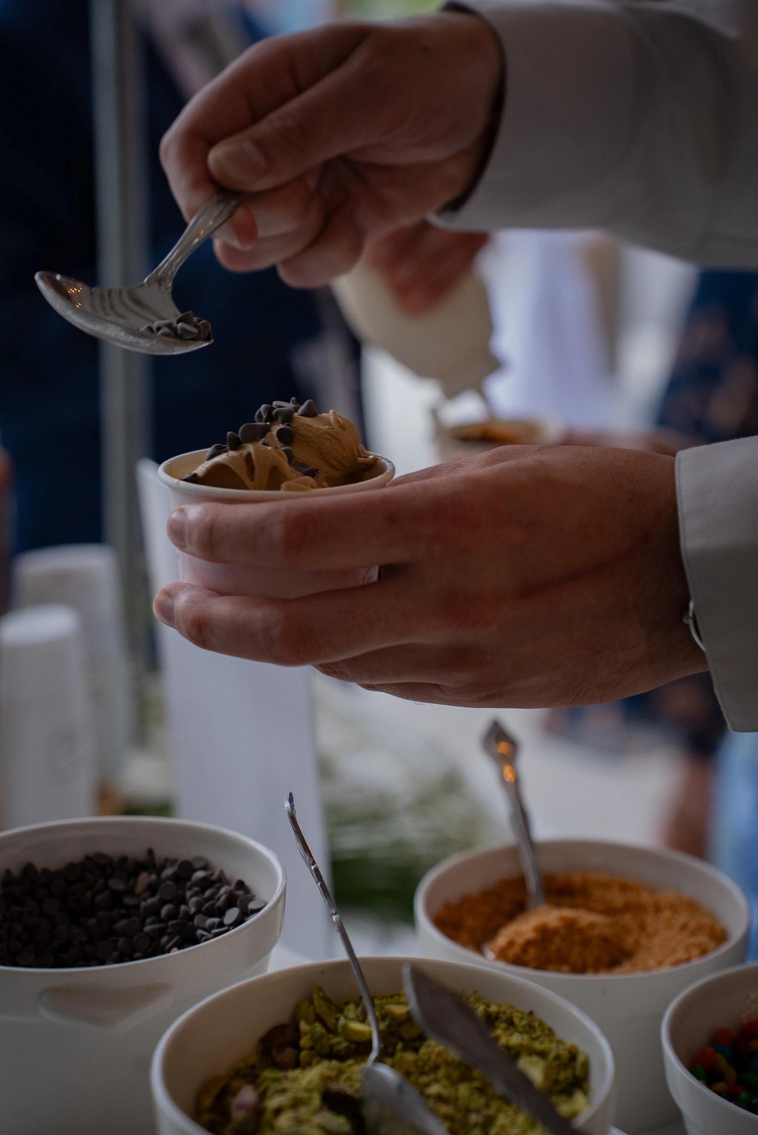 Close-up of a person using a spoon to serve chocolate ice cream from a bowl at a buffet.