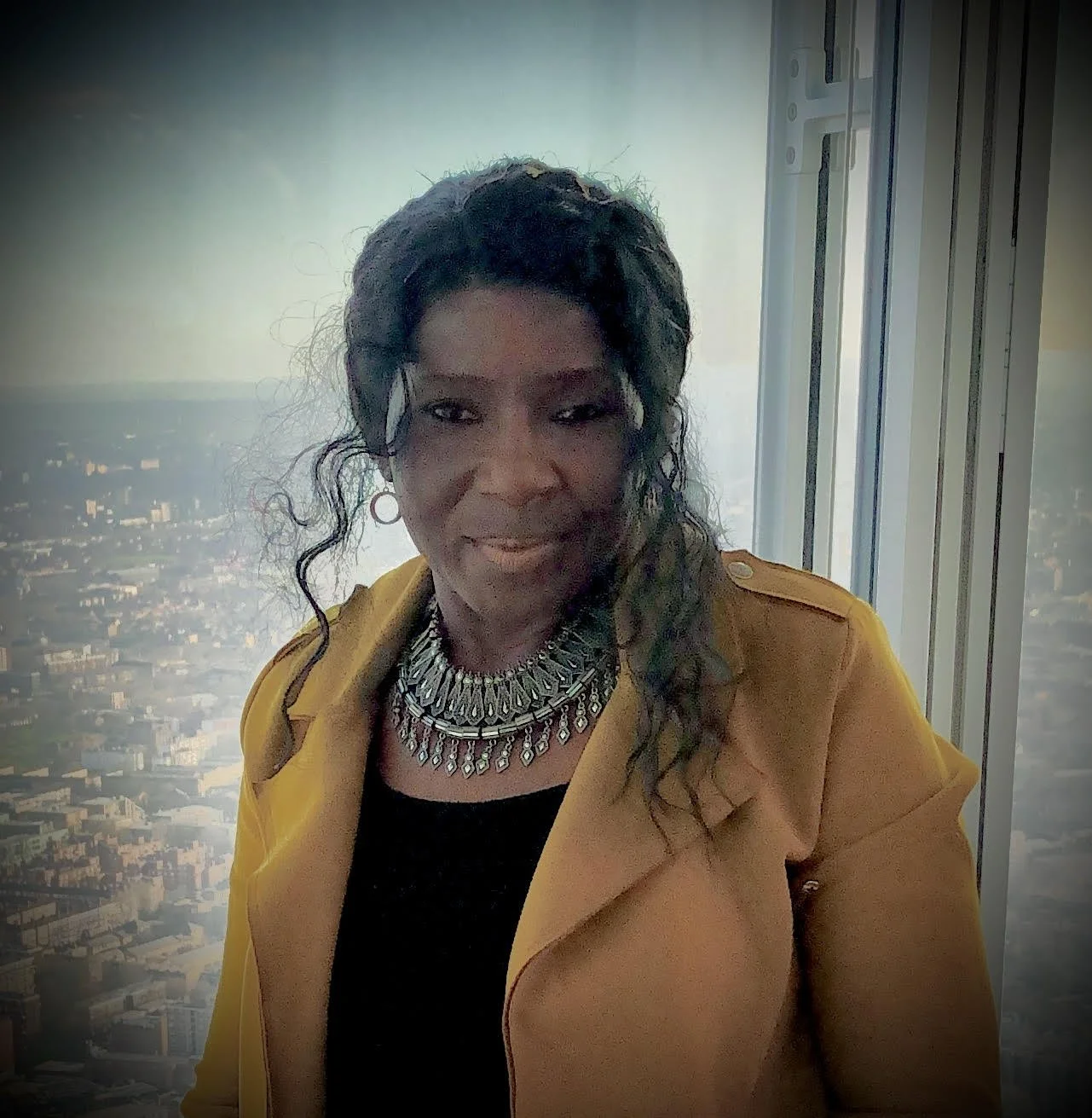 A photo of Temi Fawehinmi wearing a yellow jacket, black top and a statement silver necklace. She has curly hair and a big smile