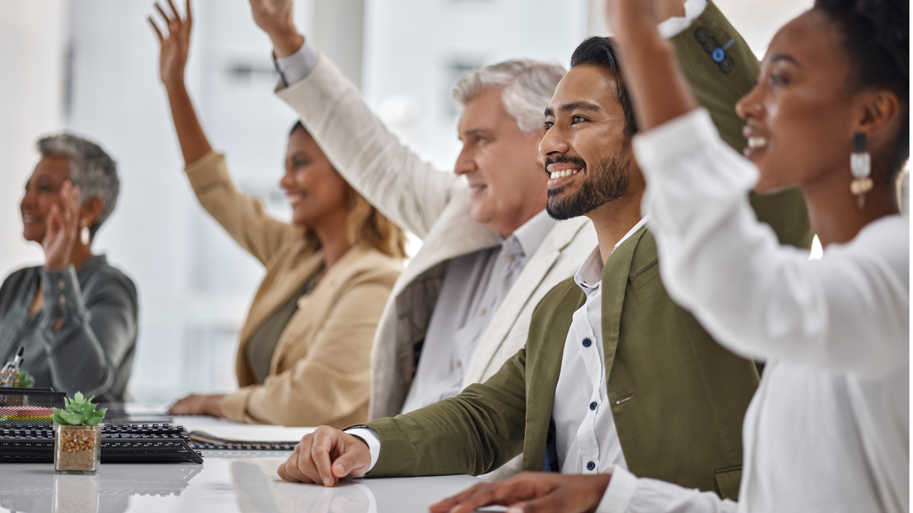 Adult learners in a training session raising their hands to respond to a question.