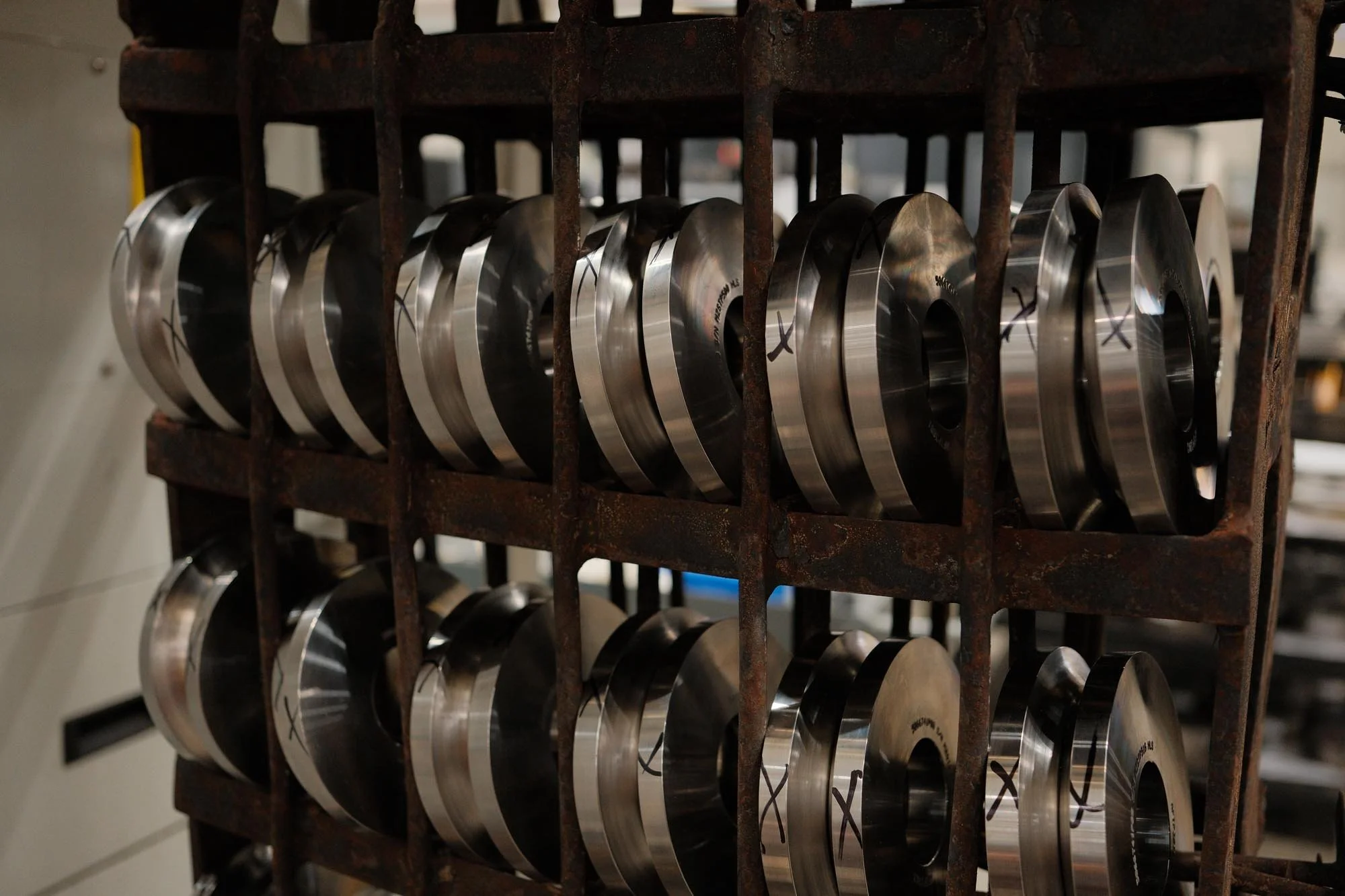 Multiple shiny metal engine pistons stored on a rusted metal rack in a workshop.