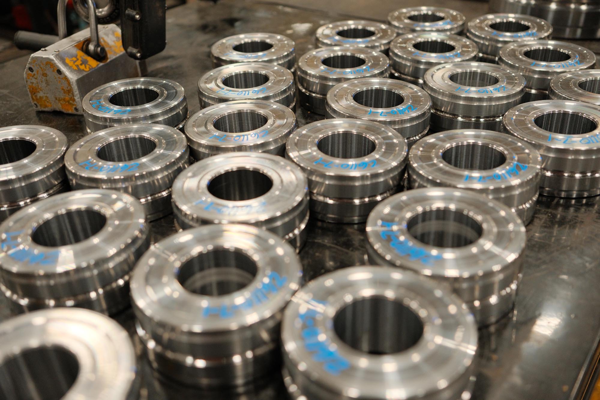 A collection of shiny metal machine parts with blue markings arranged on a work surface in a workshop.