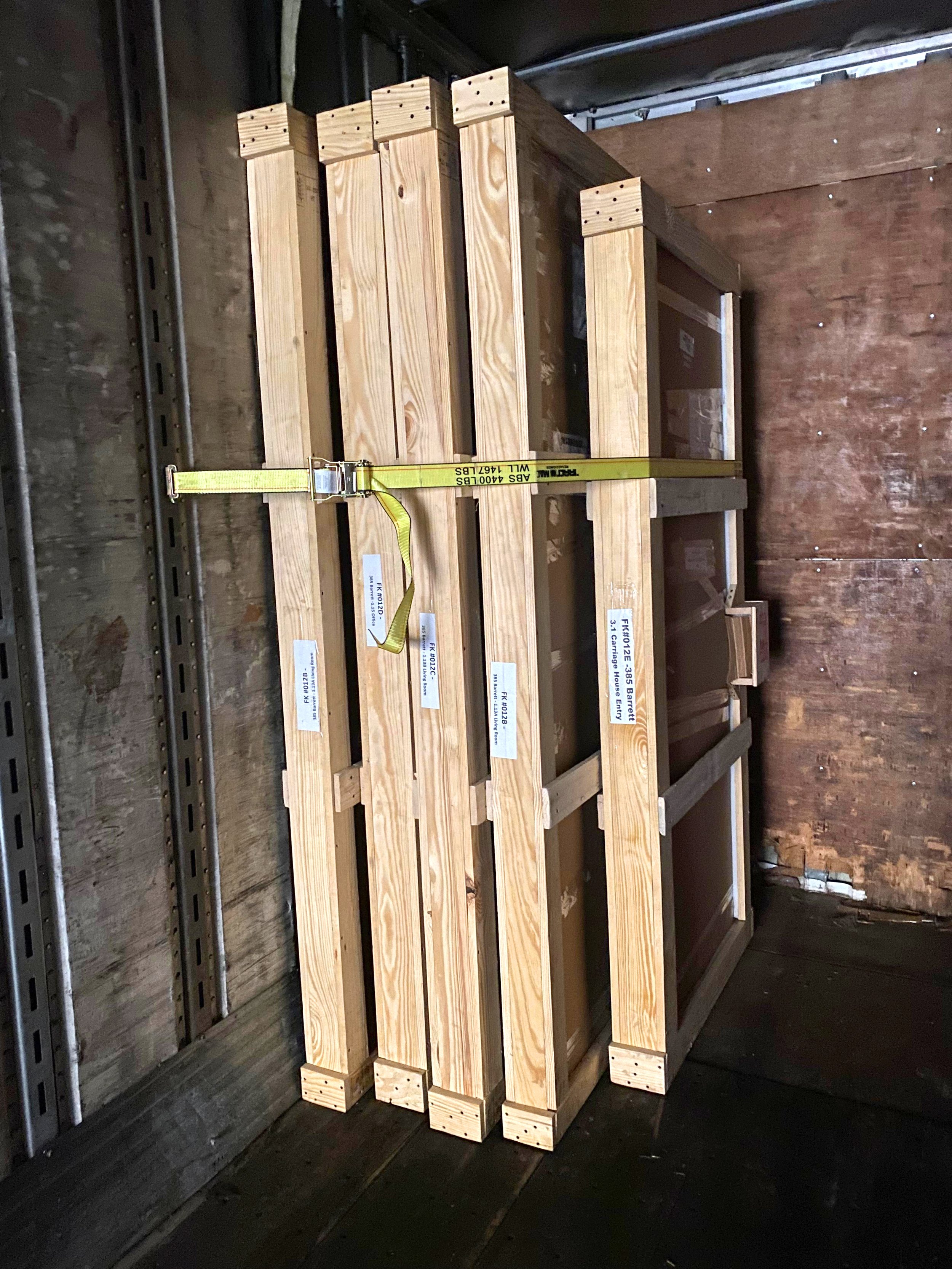Stack of wooden pallets inside a storage room with dark walls and floor, secured with a yellow strap.