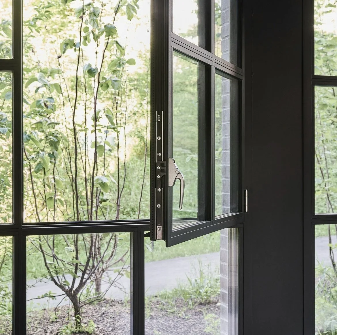 A black-framed window with an open casement, showing a view of green trees and grass outside.
