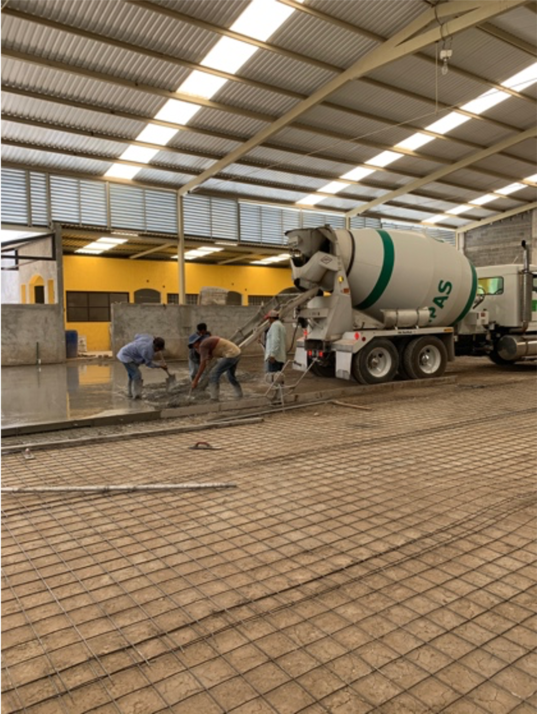 Construction workers pouring concrete on a building site with a cement mixer truck inside a large, covered structure.
