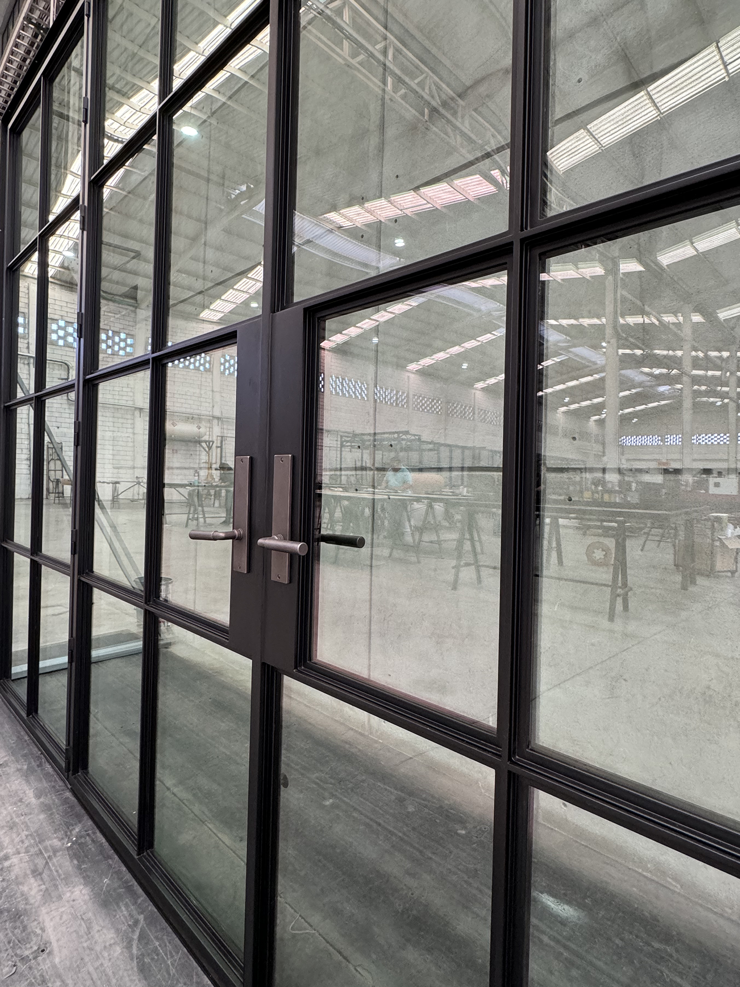 A glass door with black metal frame open, revealing an industrial-style indoor space with benches and tables visible through the glass.