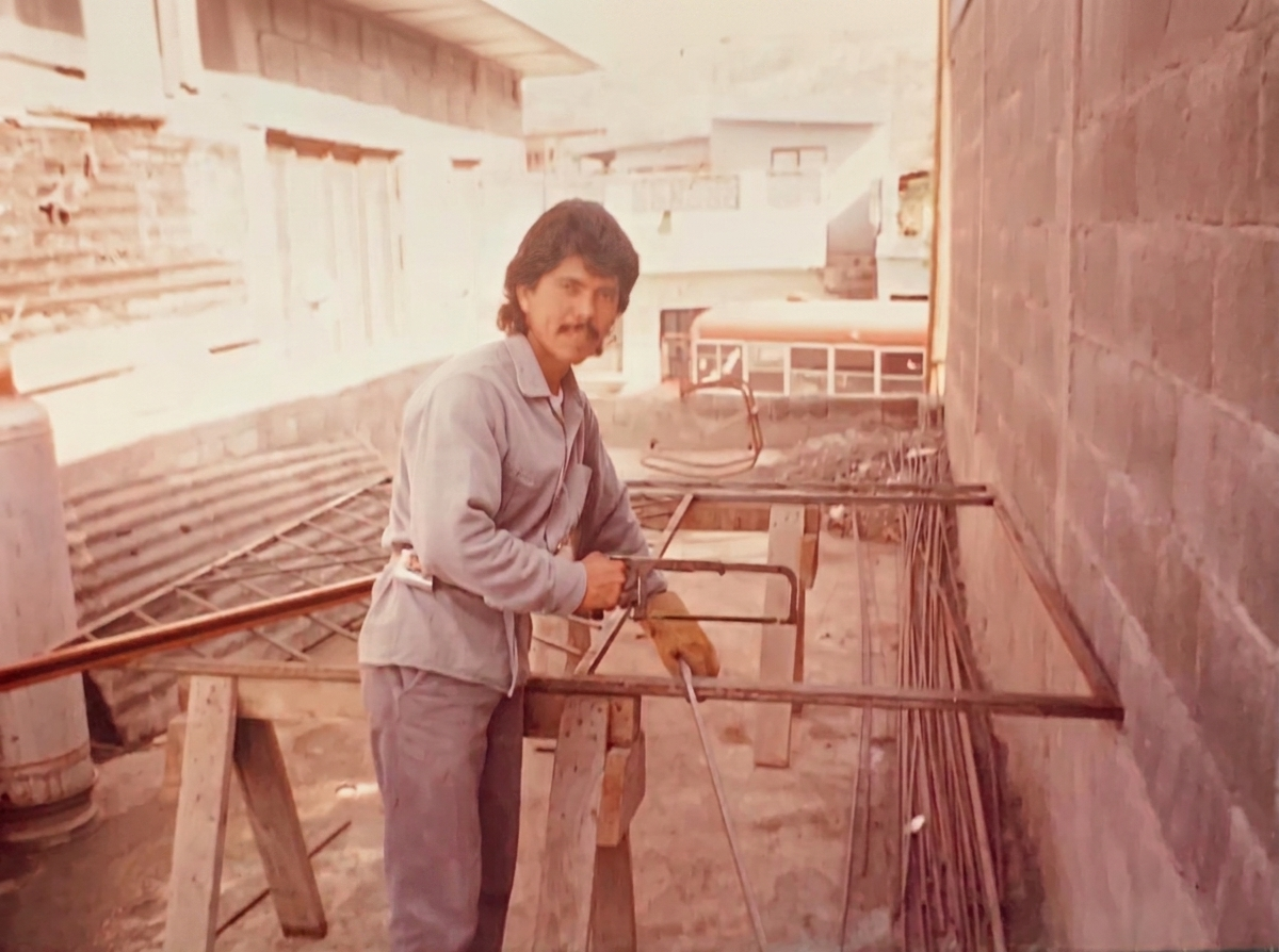 A man working on a construction site with wooden scaffolding, brick walls, and construction materials around him.