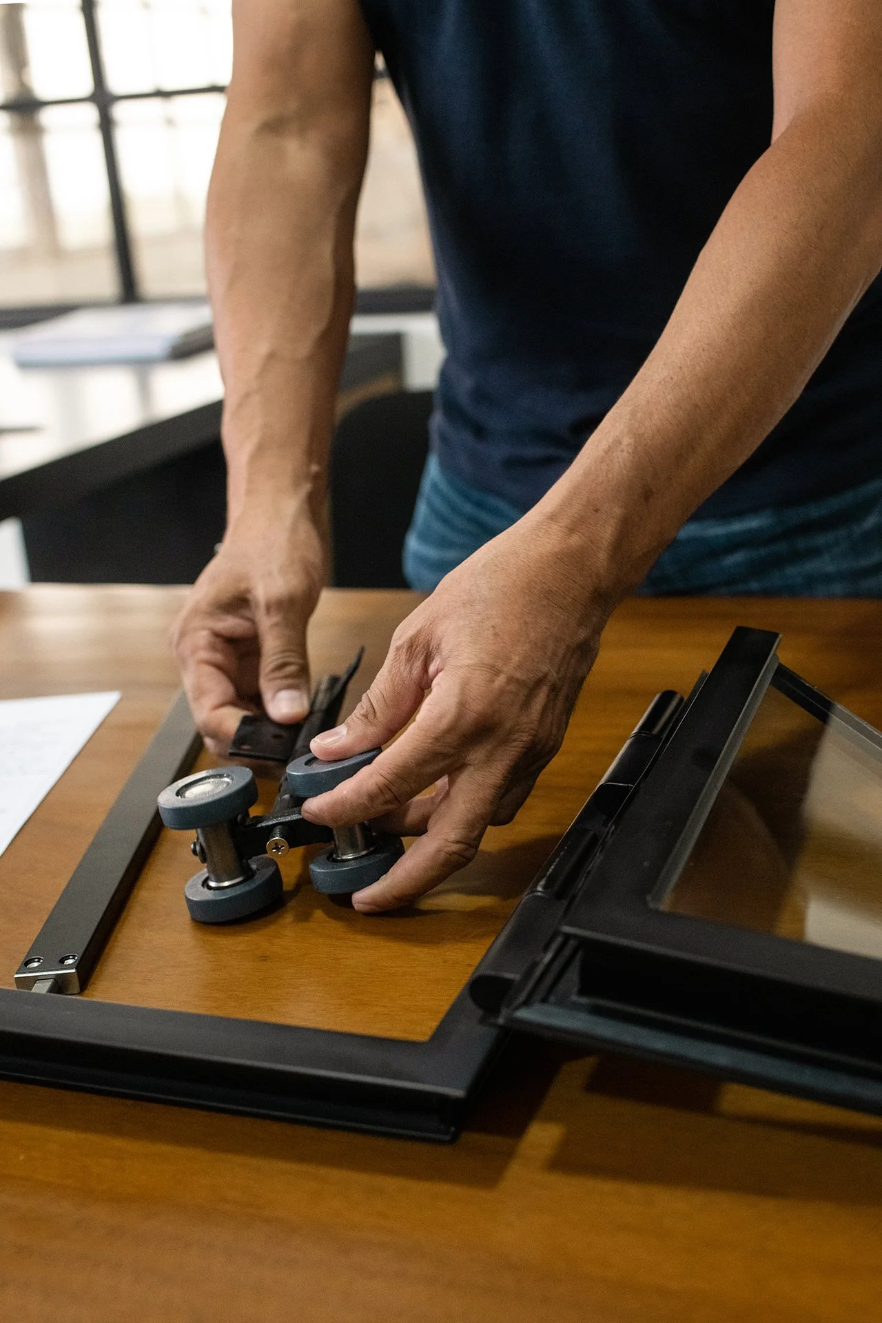 Person adjusting a camera slider on a wooden table in a room with large windows.