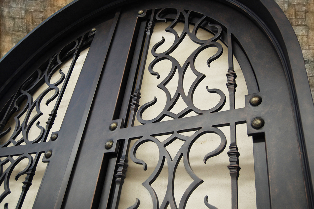Close-up of decorative wrought-iron gate with intricate scrollwork, set against a brick wall background.