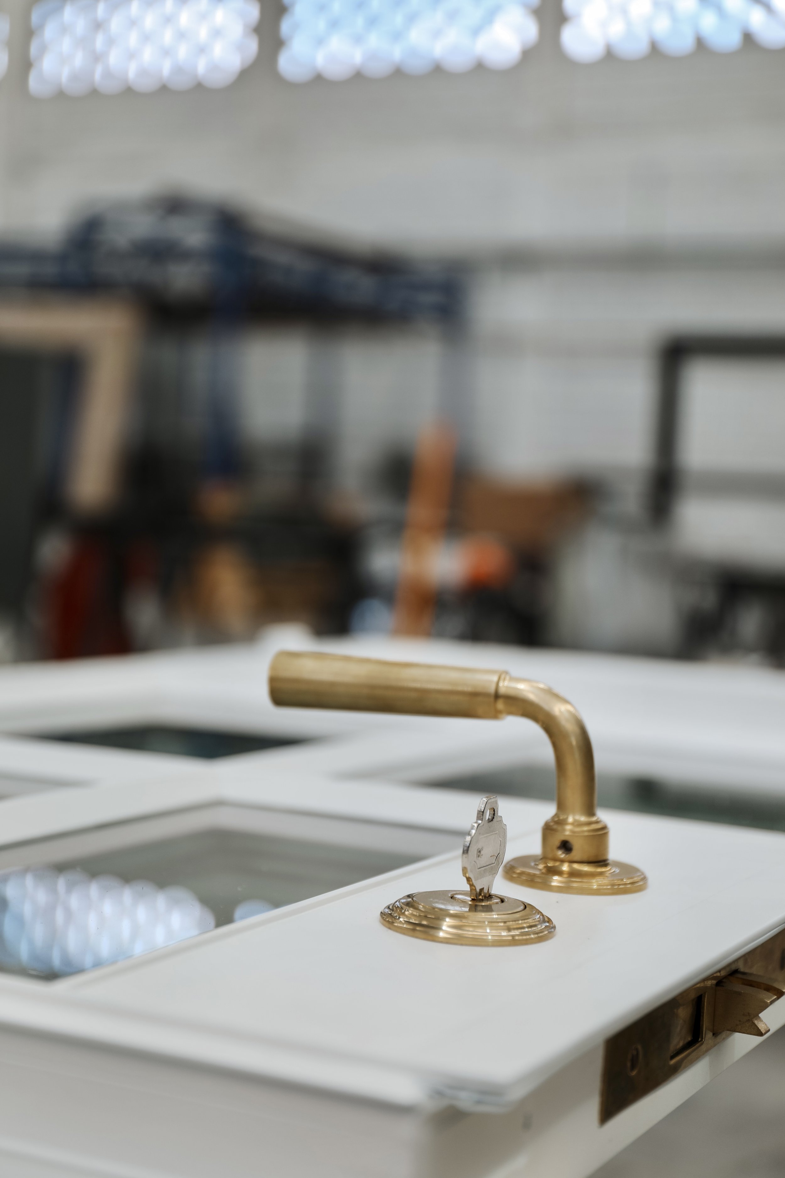 A drill press with a wooden handle attached to the front of the machine, situated in a workshop or garage setting.