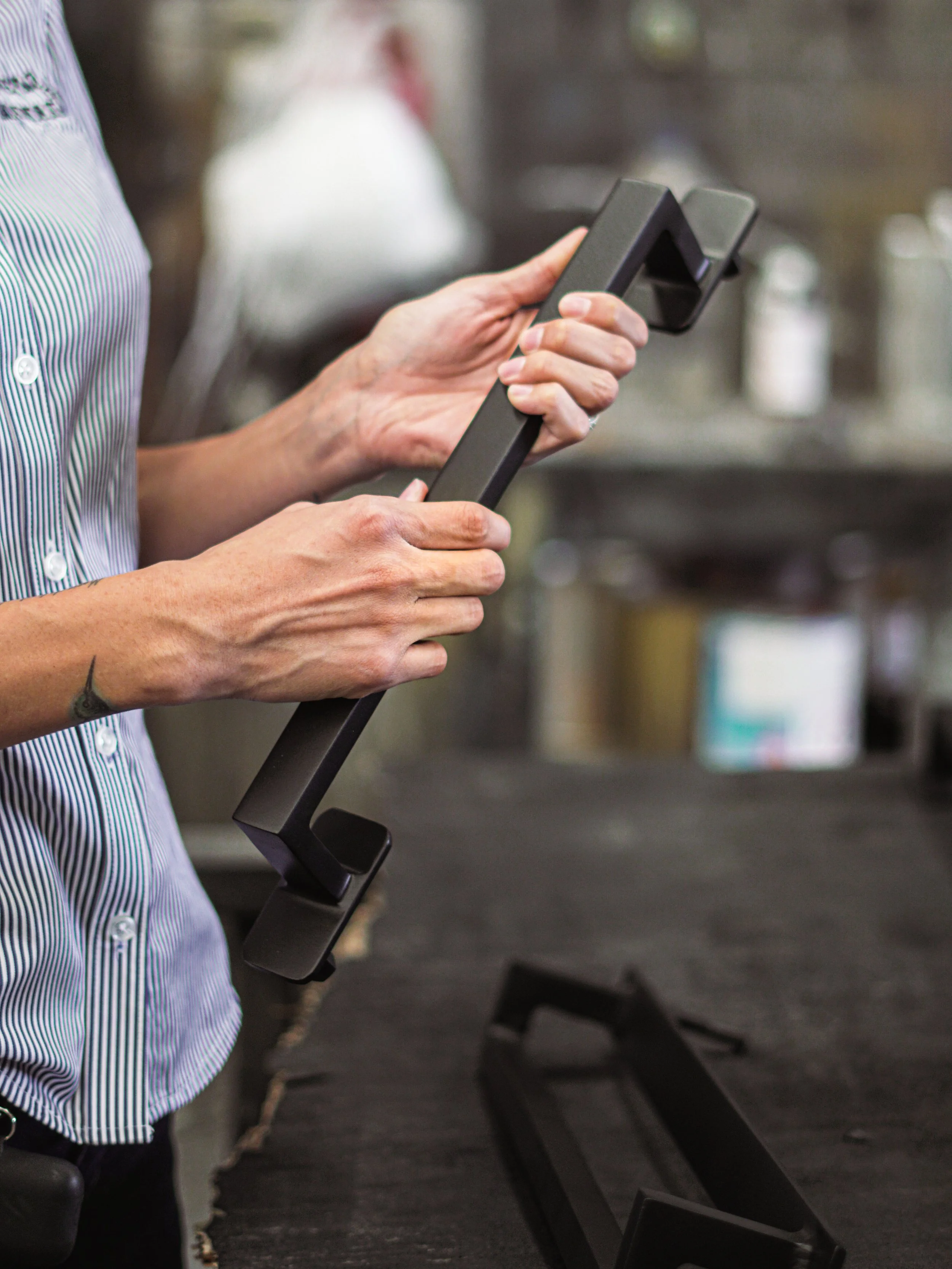 A person wearing a striped shirt holding a black handheld device in a kitchen or workspace setting.